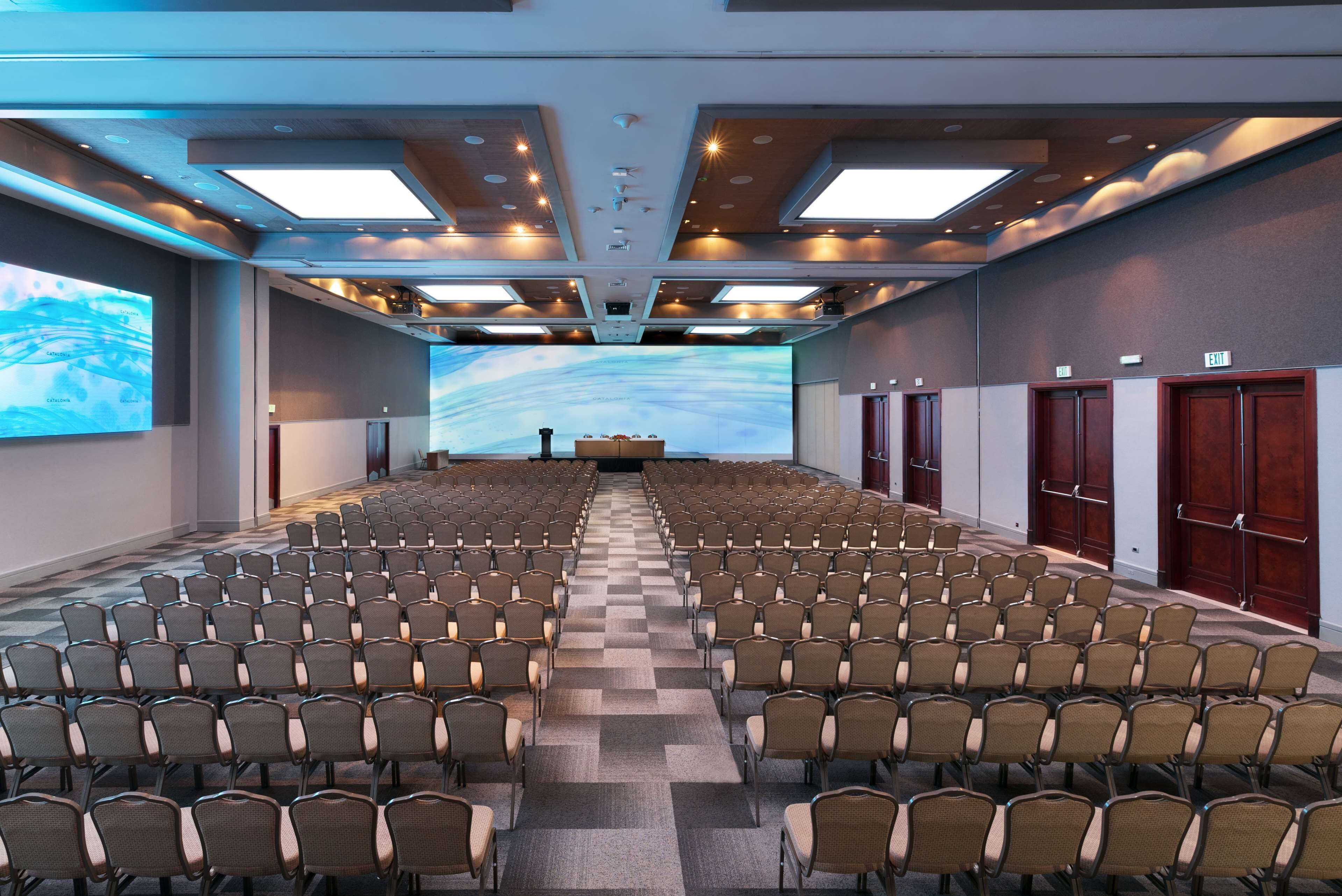 A conference room with rows of chairs, a large screen, and a podium.