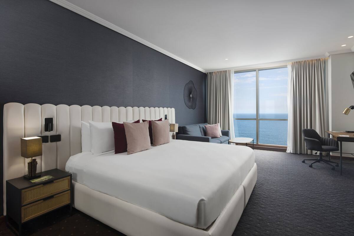 Une chambre d’hôtel moderne avec un grand lit, un bureau, une chaise et une vue sur l’océan.