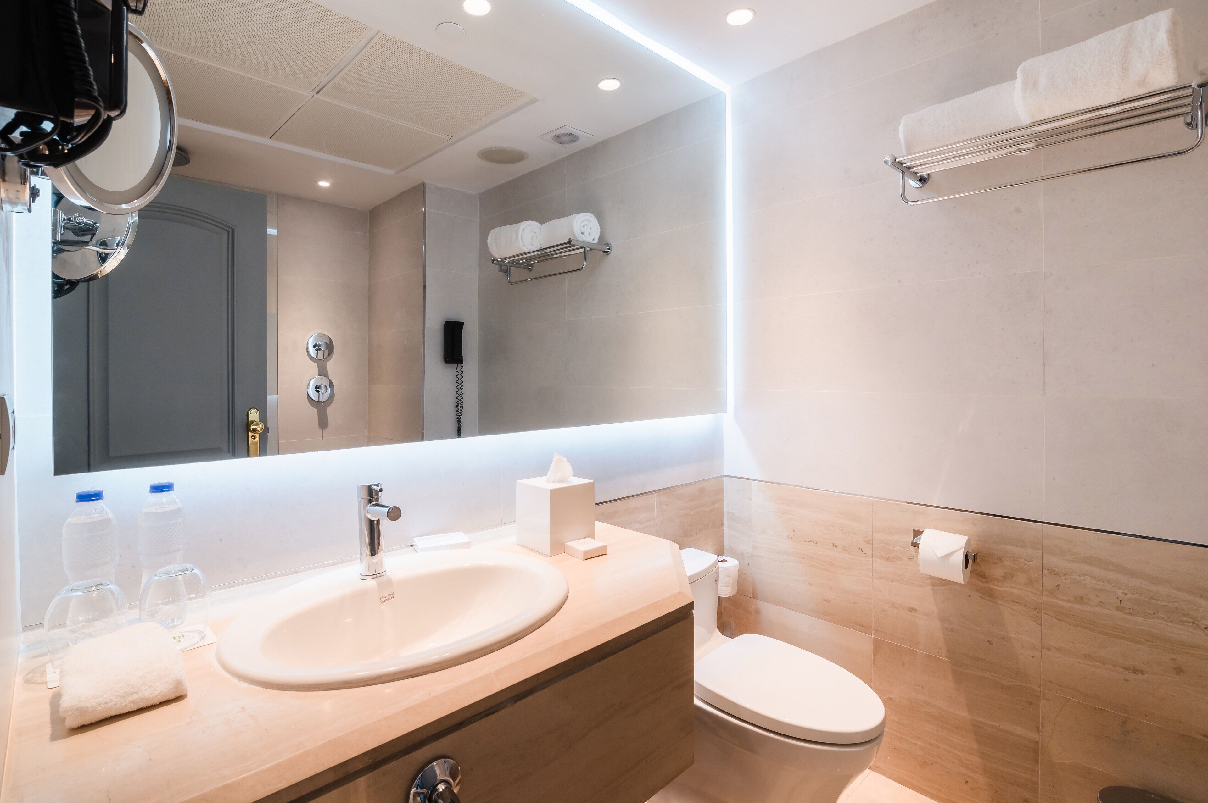 A modern bathroom with a large mirror, a sink, a toilet, and a towel rack.