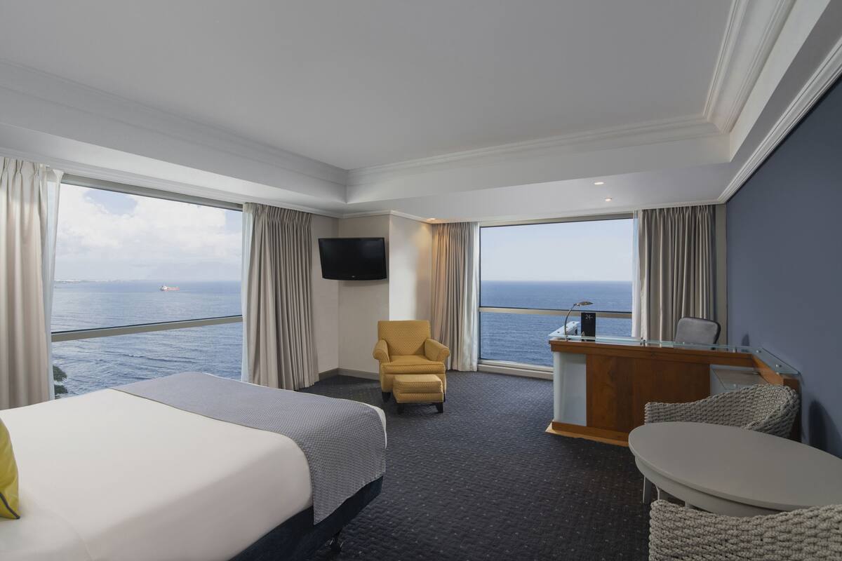 Une chambre d’hôtel avec un lit, un bureau, une chaise, une télévision et une vue sur la mer.