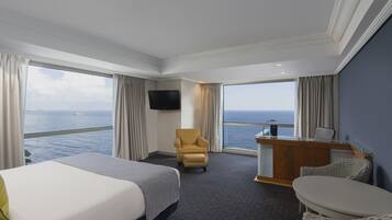 A hotel room with a bed, a desk, a chair, a TV, and a view of the sea.