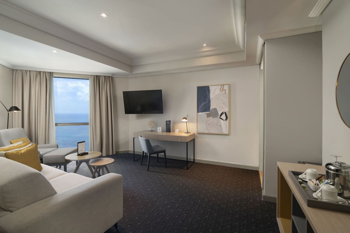 Une chambre d’hôtel dotée d’une grande fenêtre, d’un bureau, d’une chaise, d’un canapé et d’un coin repas avec un plateau contenant divers éléments pour le petit-déjeuner.