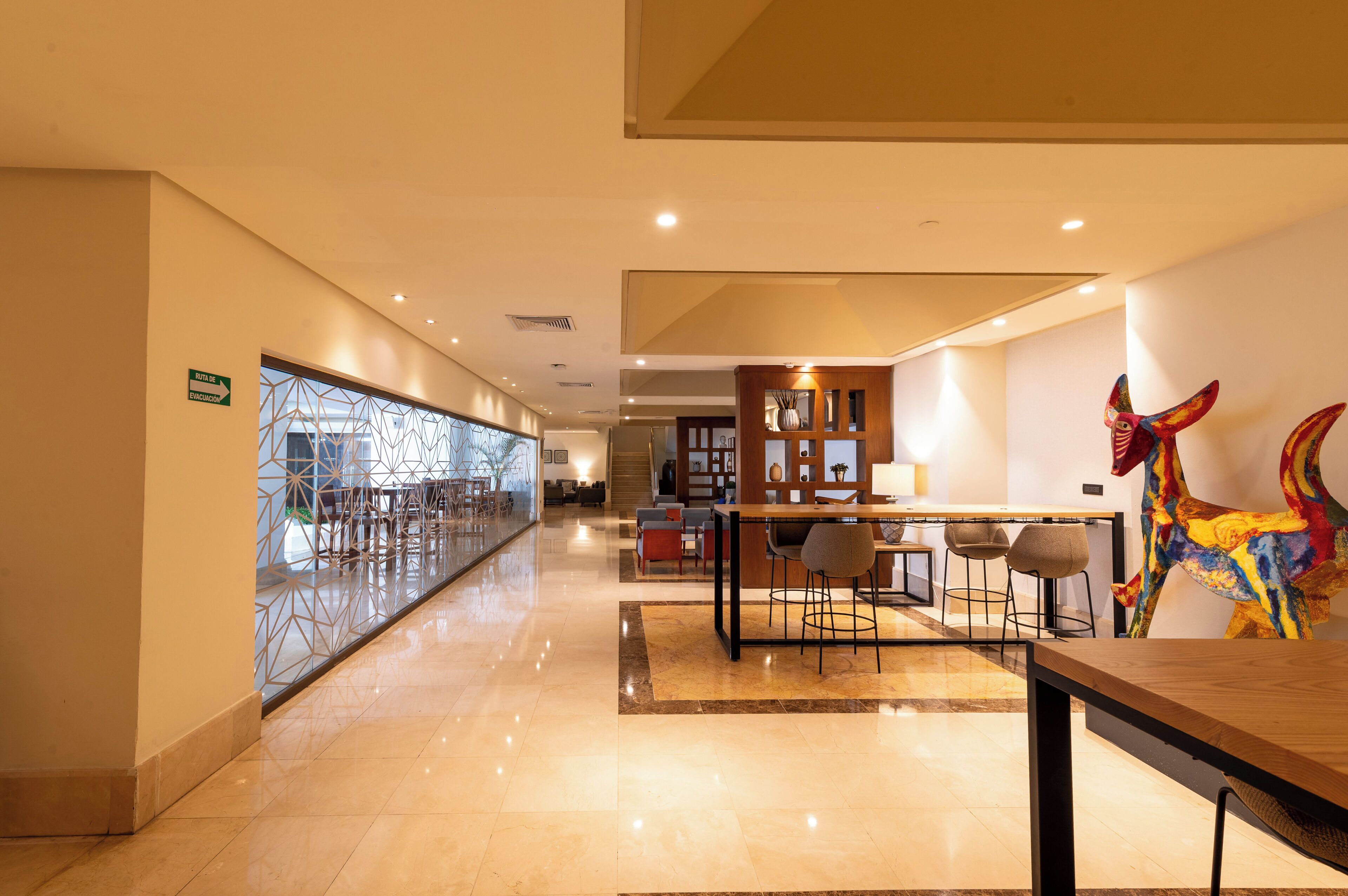 A hotel lobby with a long corridor, a reception desk, and a colorful dinosaur sculpture.