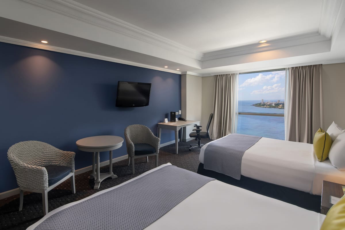 Une chambre d’hôtel avec deux lits, un bureau, une chaise, une télévision et une vue sur la mer.