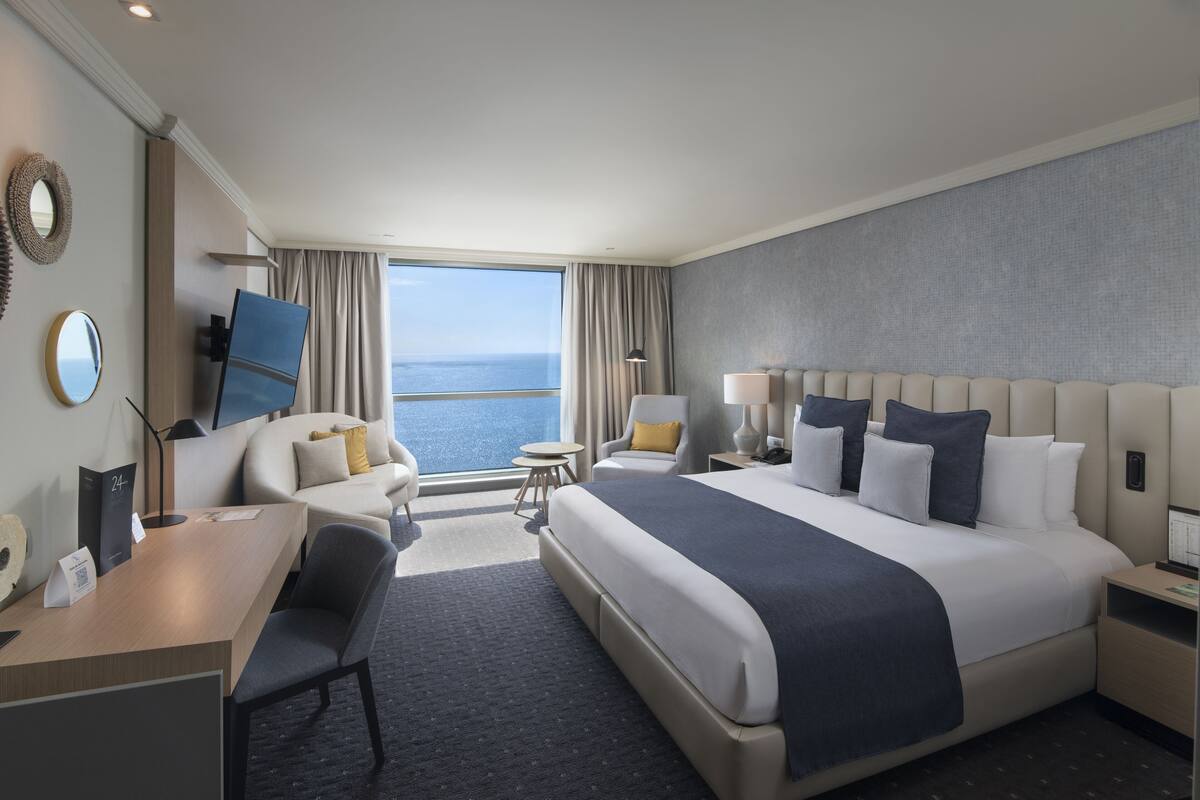 Une chambre d’hôtel avec un grand lit, un bureau, une chaise, une télévision et une vue sur l’océan.