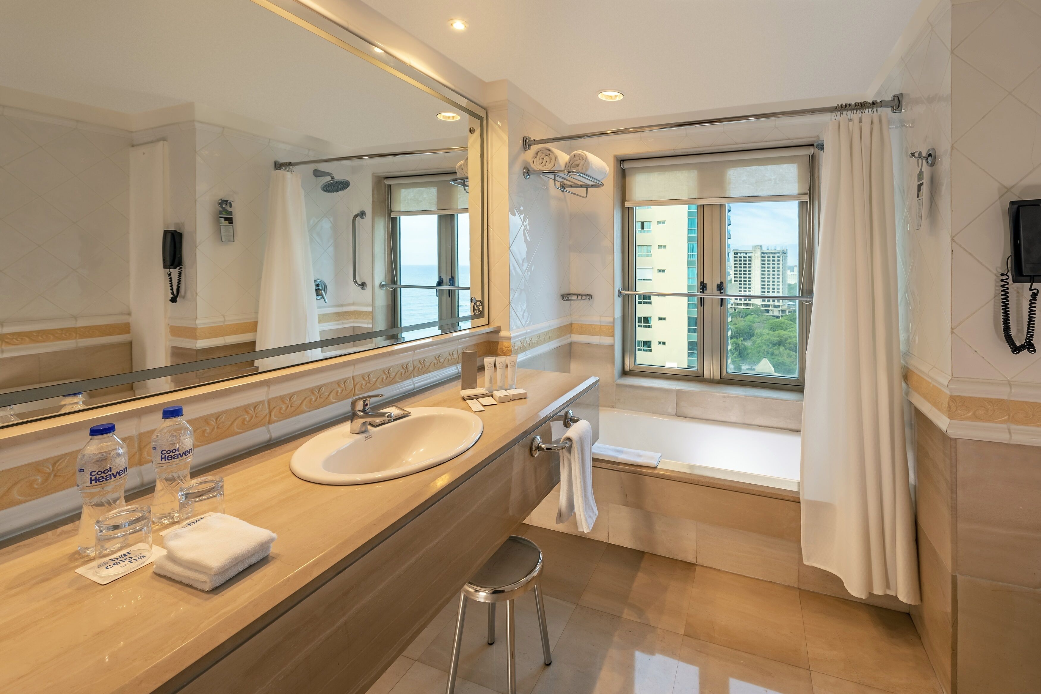 A modern bathroom with a large mirror, a sink, a bathtub, and a window with a view of buildings.