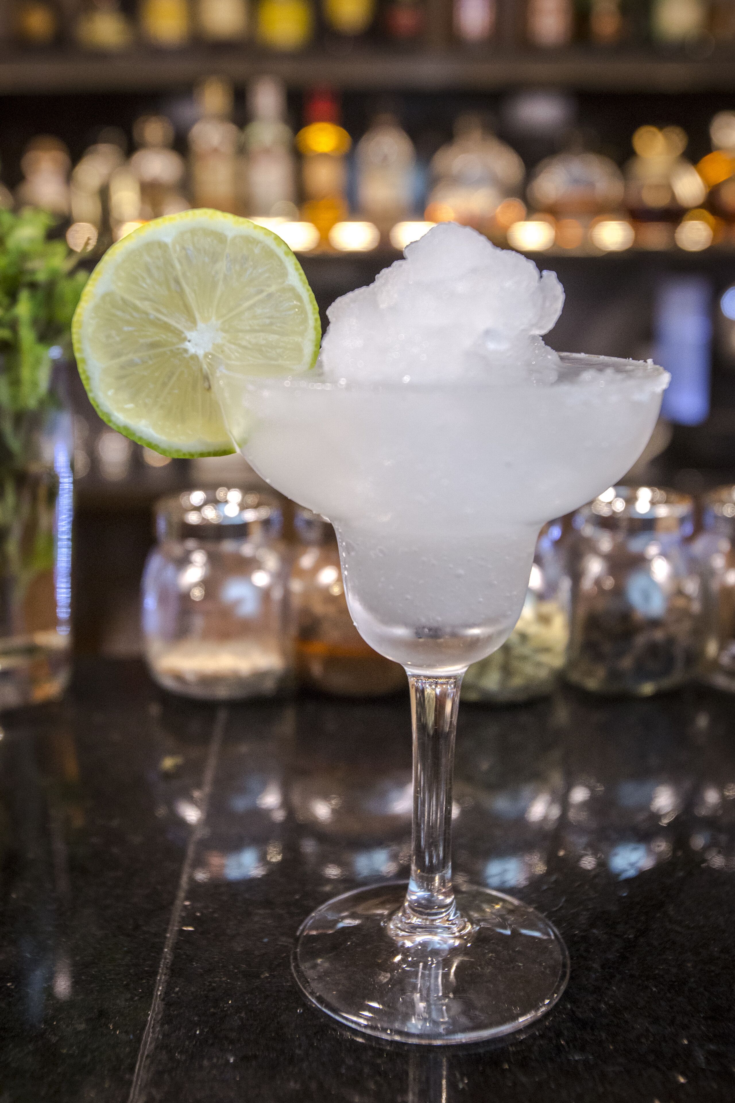 A cocktail glass with ice and a lime slice on a bar counter.