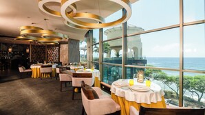 Een restaurant met ronde tafels, gele tafelkleden en uitzicht op zee.