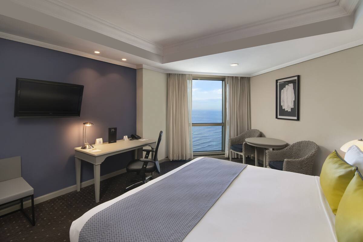 Une chambre d’hôtel avec un lit, un bureau, une chaise et une vue sur l’océan.