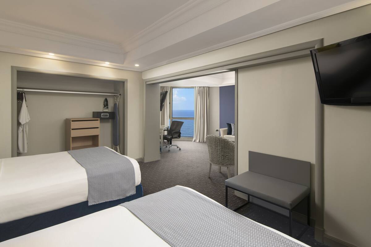 Une chambre d’hôtel avec deux lits, un bureau, une chaise, une télévision et une vue sur la mer.