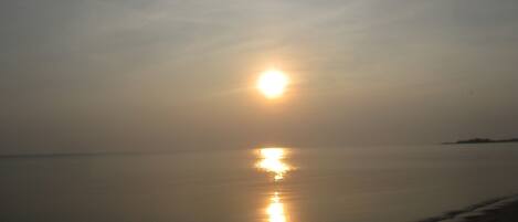 Ein ruhiger Strand bei Sonnenuntergang, wobei sich die Sonne im Wasser spiegelt.