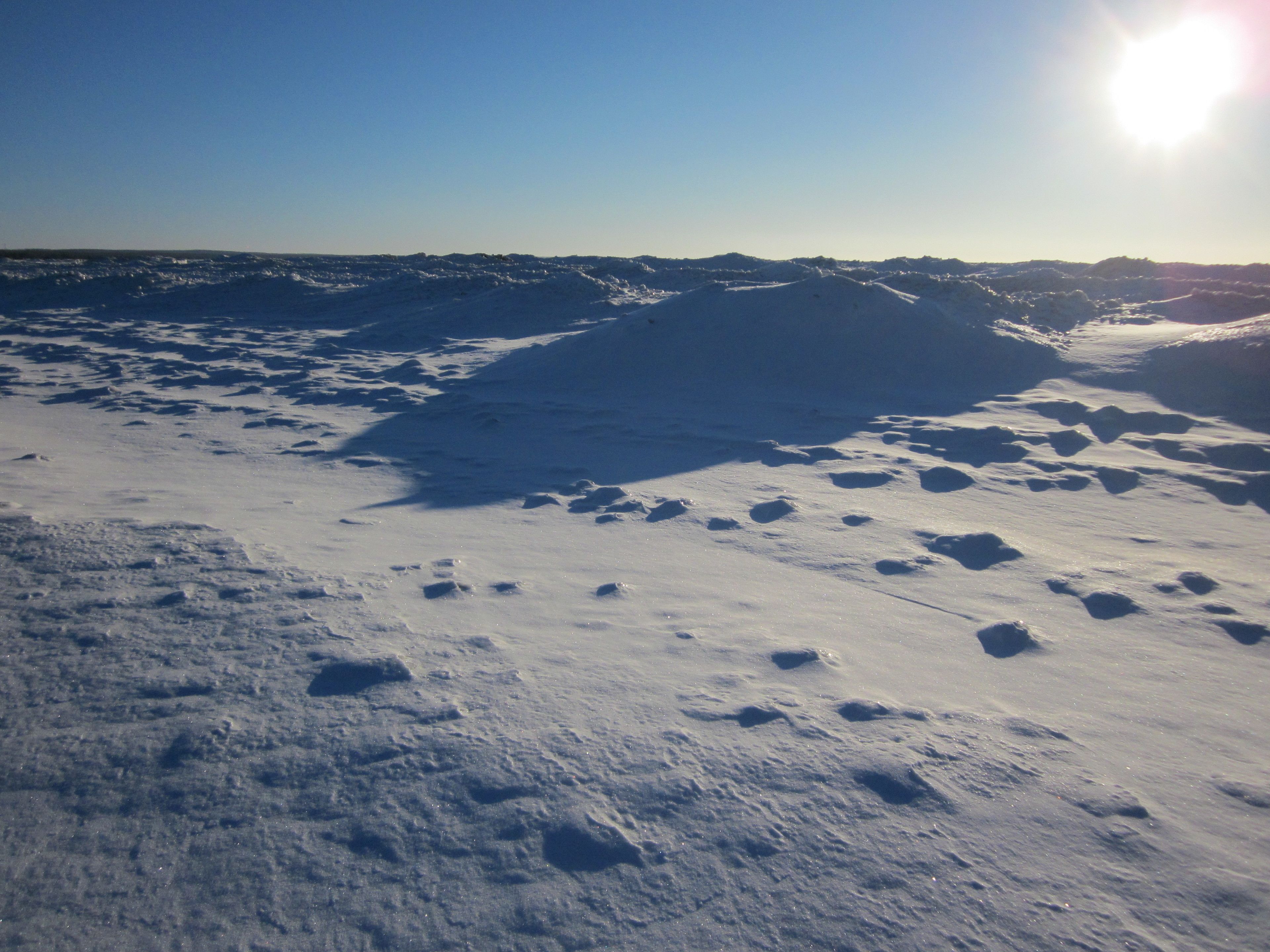 A snowy landscape with undulating terrain and a clear sky.