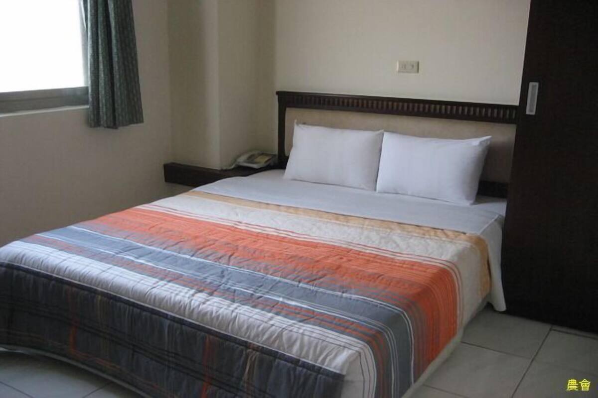 A hotel room with a bed, a nightstand, a telephone, and a window with curtains.