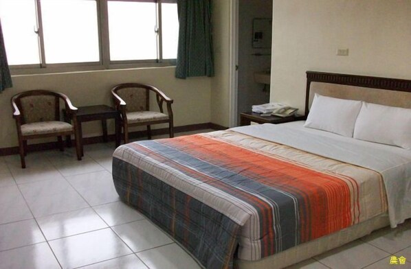 A bedroom with a bed, two chairs, a bedside table, and a window with curtains. - Penghu Farmers Association Resort (Magong)