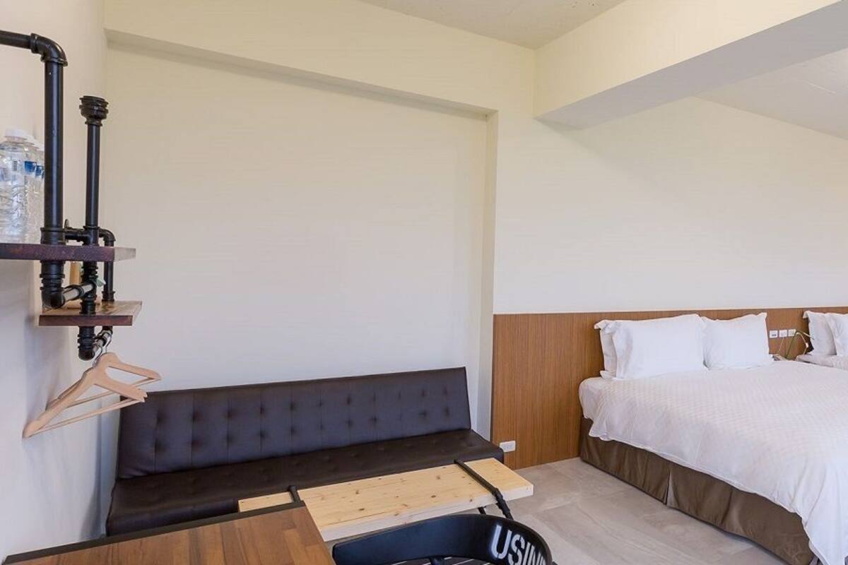 Una habitación de hotel moderna con una cama, cabecera de madera, un banco y un escritorio con silla.