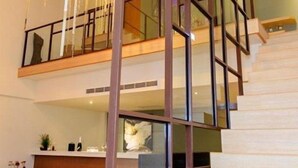 Un interior moderno con una escalera que conduce a un segundo piso, un candelabro y una zona de cocina.