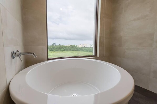 Une salle de bain moderne avec une baignoire sur pieds, une fenêtre et une vue sur la verdure et les bâtiments.