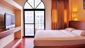 A hotel room with a bed, a television on a wooden dresser, a large window with curtains, and a view of buildings outside. - Kenting Culture Resort (Hengchun)