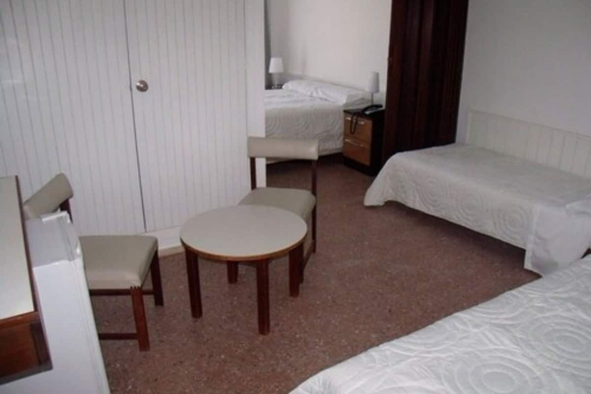 A hotel room with two single beds, a small round table, and a chair.