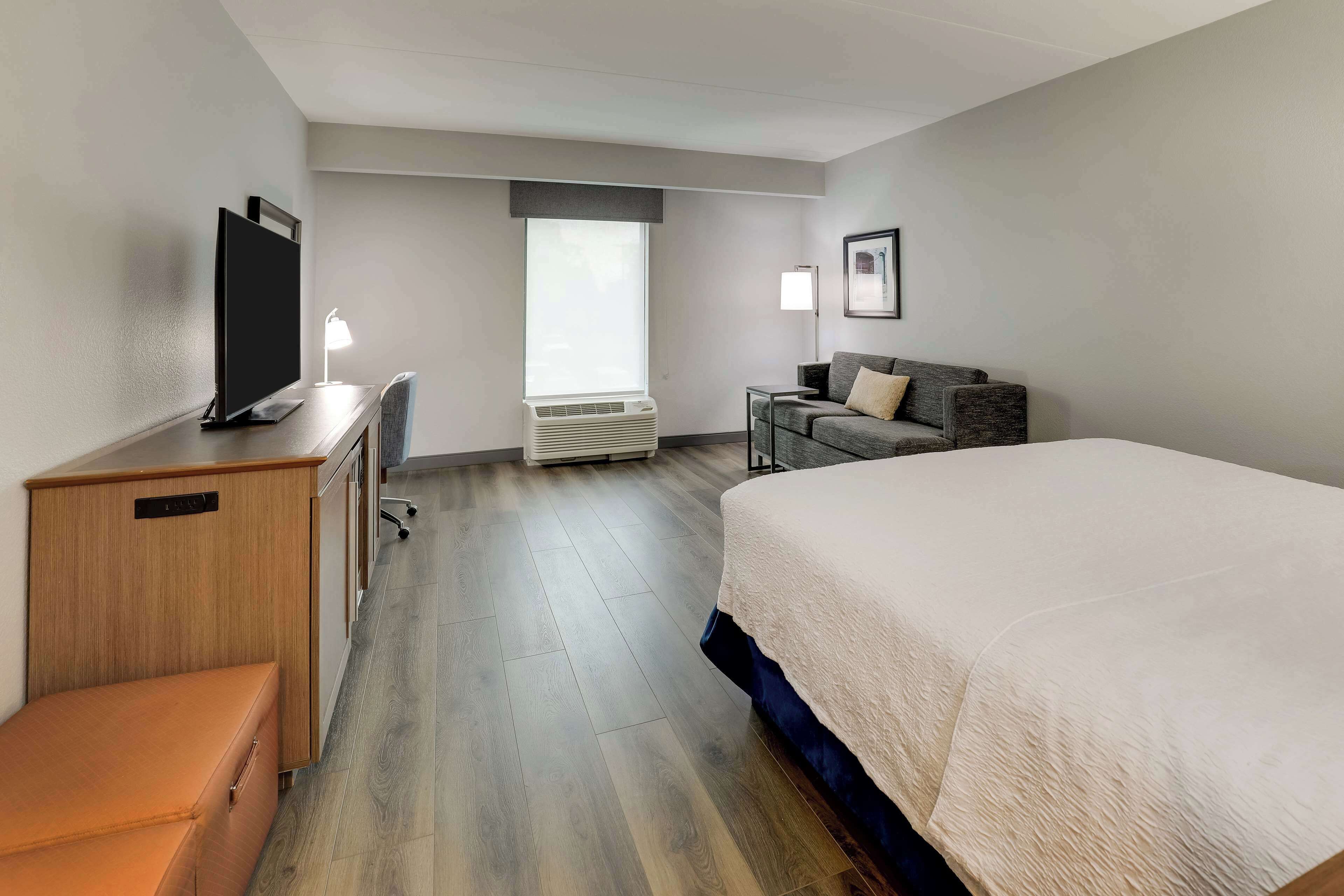 A hotel room with a bed, a desk with a TV, a chair, a couch, and a window.