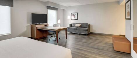 A hotel room with a bed, a desk, a television, a sofa, and a small table.