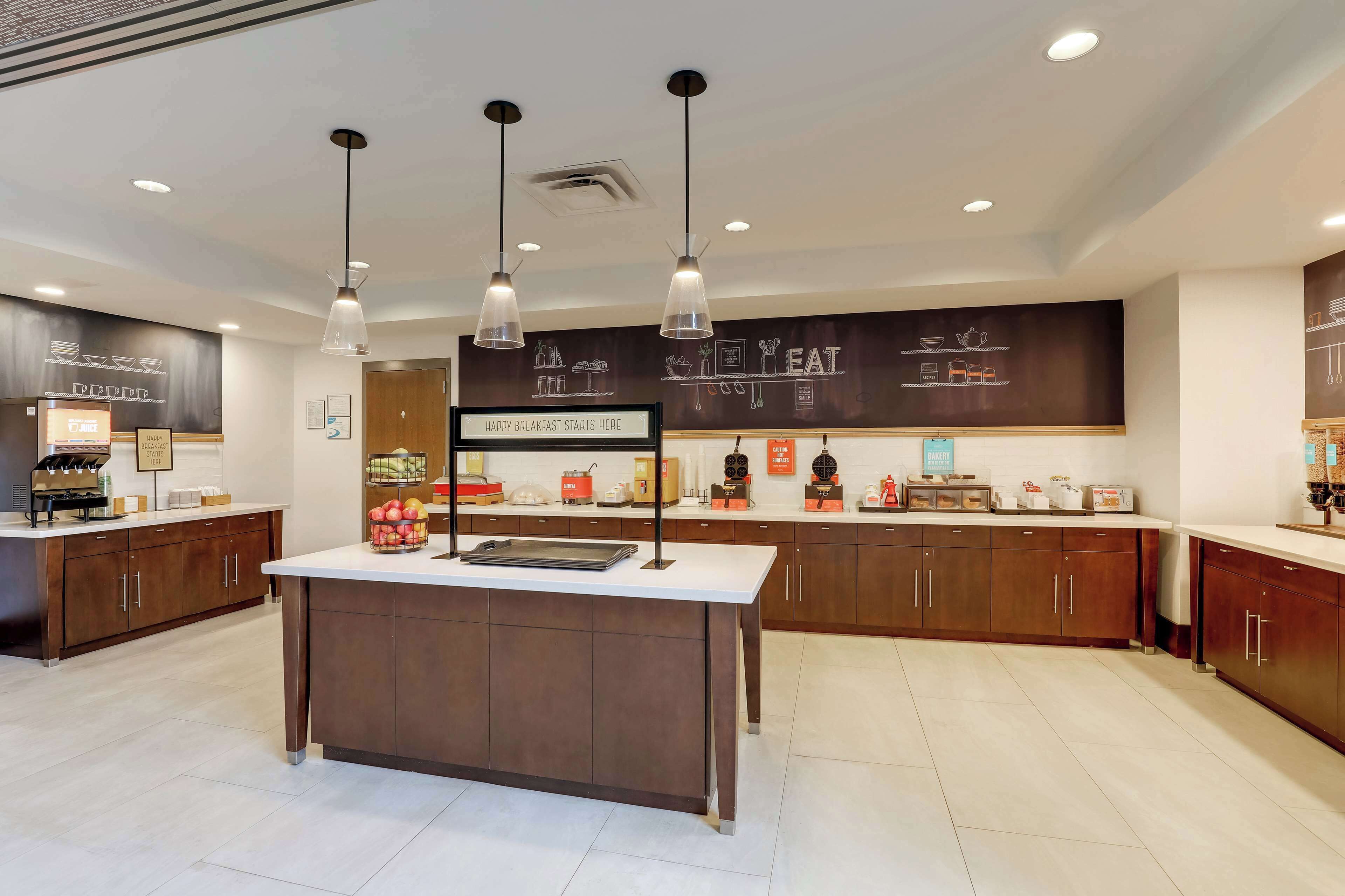 A modern kitchen area with a central island, pendant lighting, and a chalkboard with food illustrations.