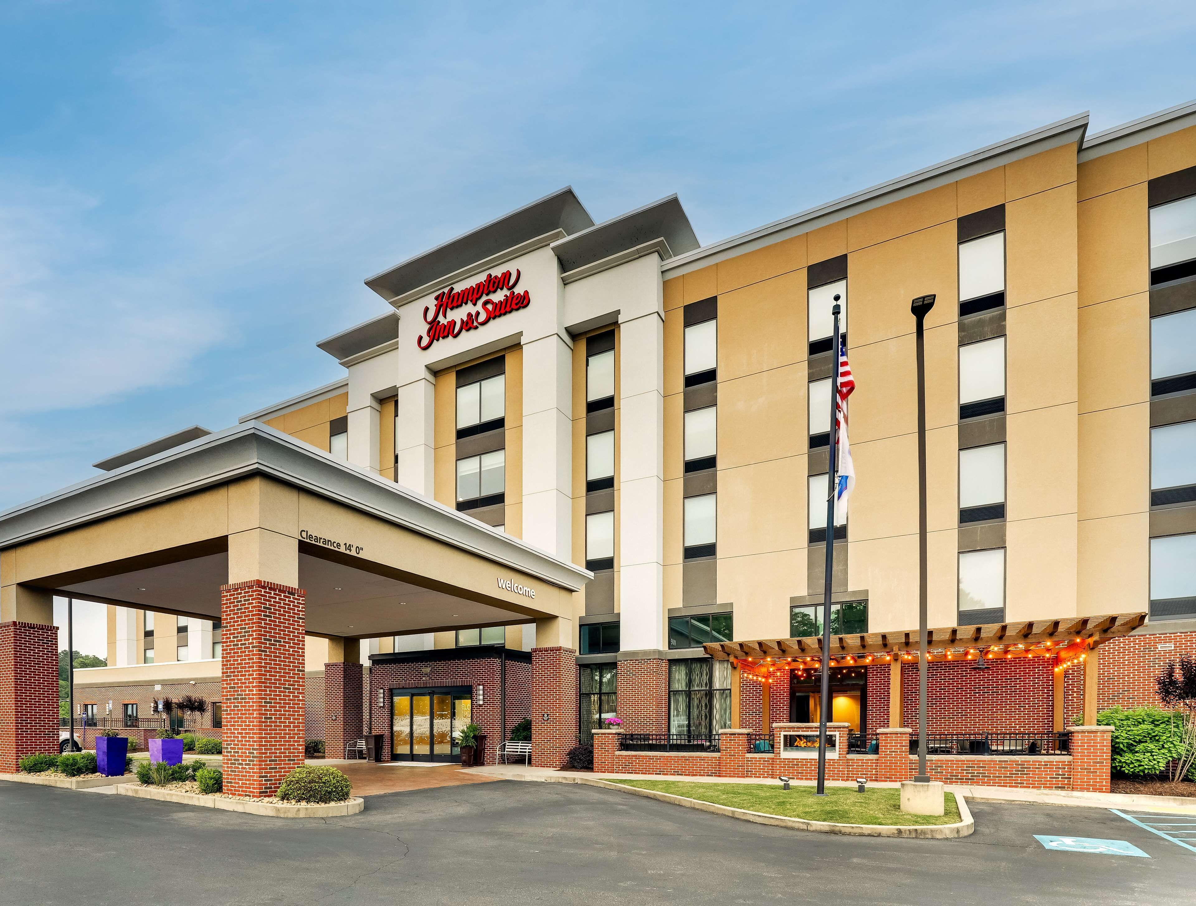 Edificio de Hampton Inn & Suites con fachada de ladrillo, entrada cubierta y un patio con luces colgantes.