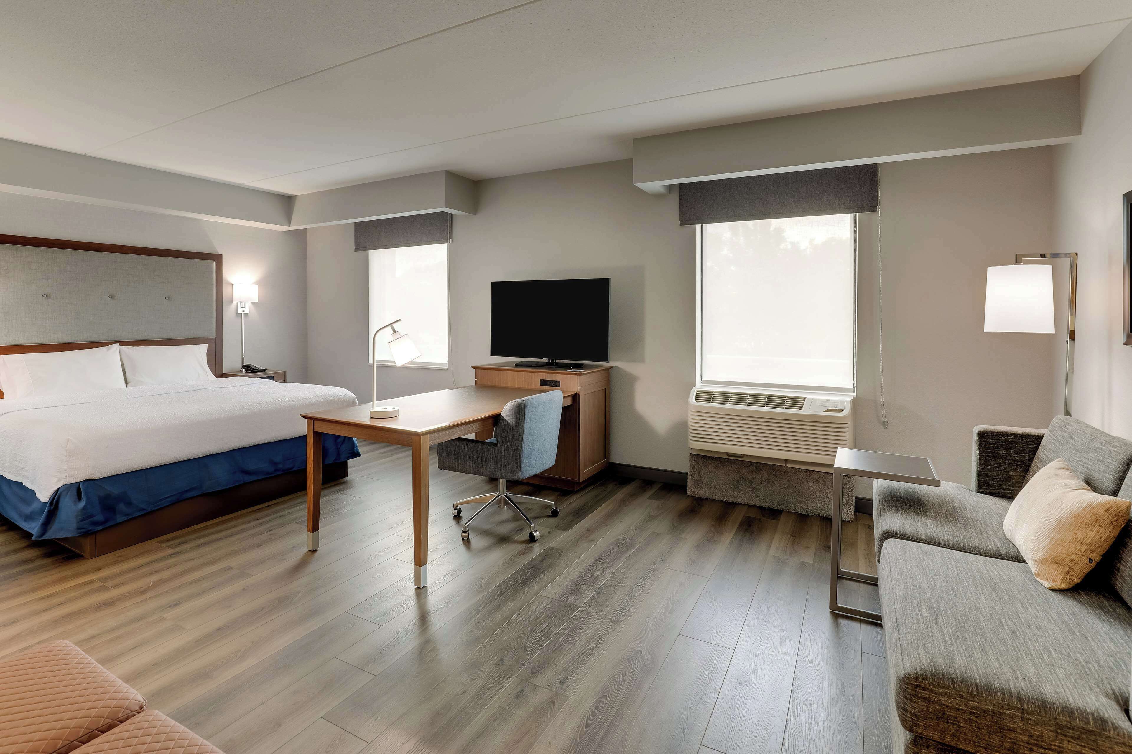 A hotel room with a bed, desk, TV, and seating area.