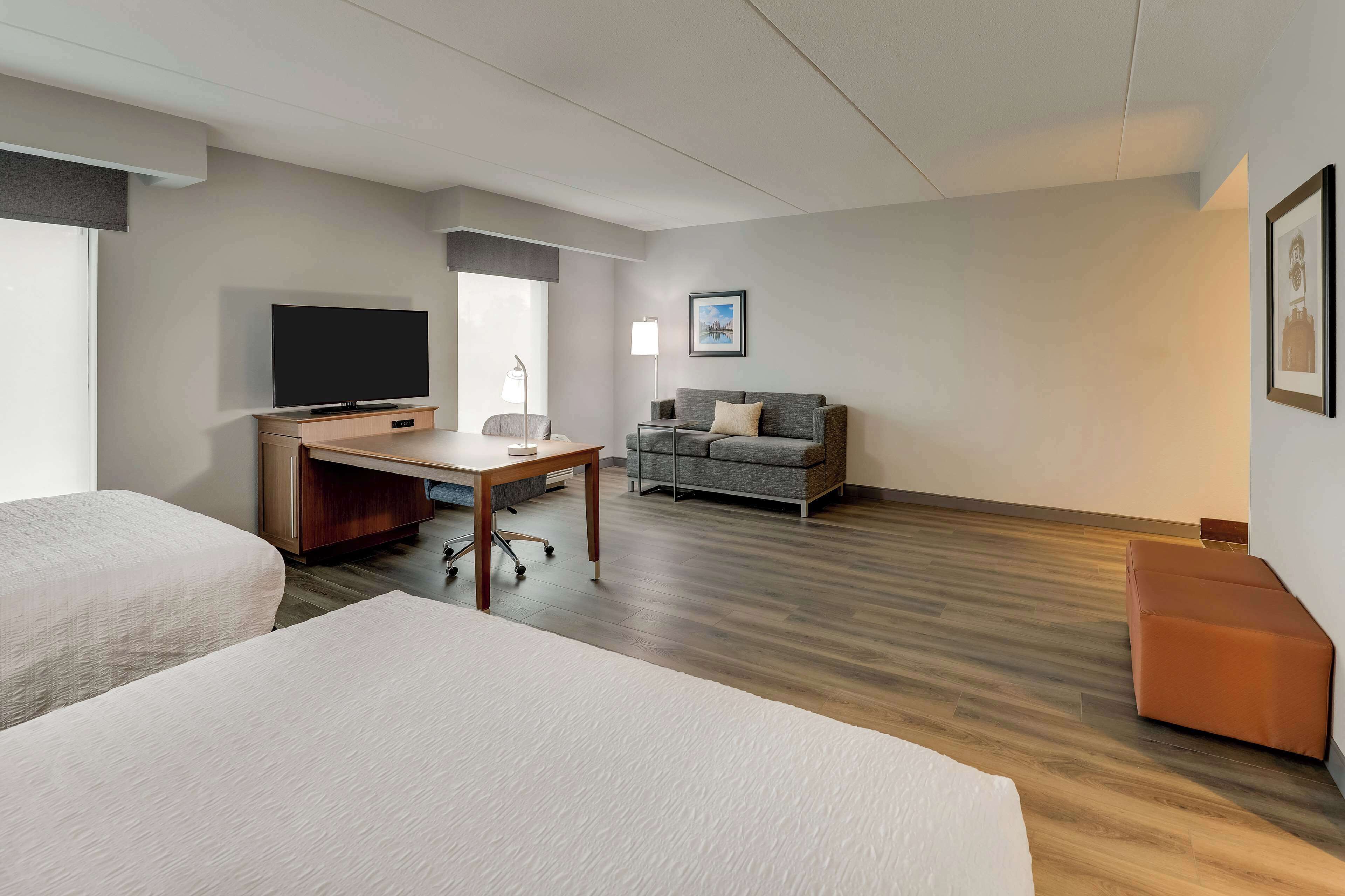 A hotel room with two beds, a desk with a TV, a sofa, and a framed picture on the wall.