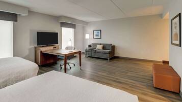A hotel room with two beds, a desk with a TV, a sofa, and a framed picture on the wall.
