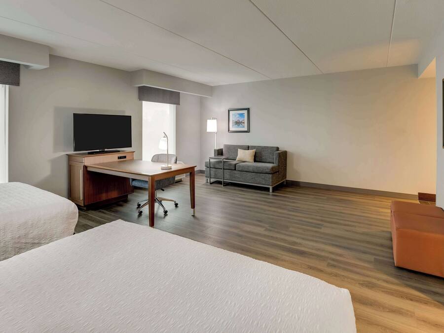 A hotel room with two beds, a desk with a TV, a sofa, and a framed picture on the wall.