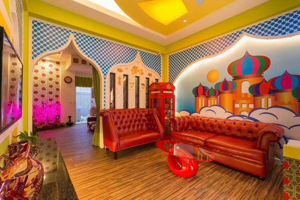 A vibrant room with a red sofa, a glass coffee table, and a decorative wall with a colorful mural. - Ali Ba Ba B&B I (Hualien City)