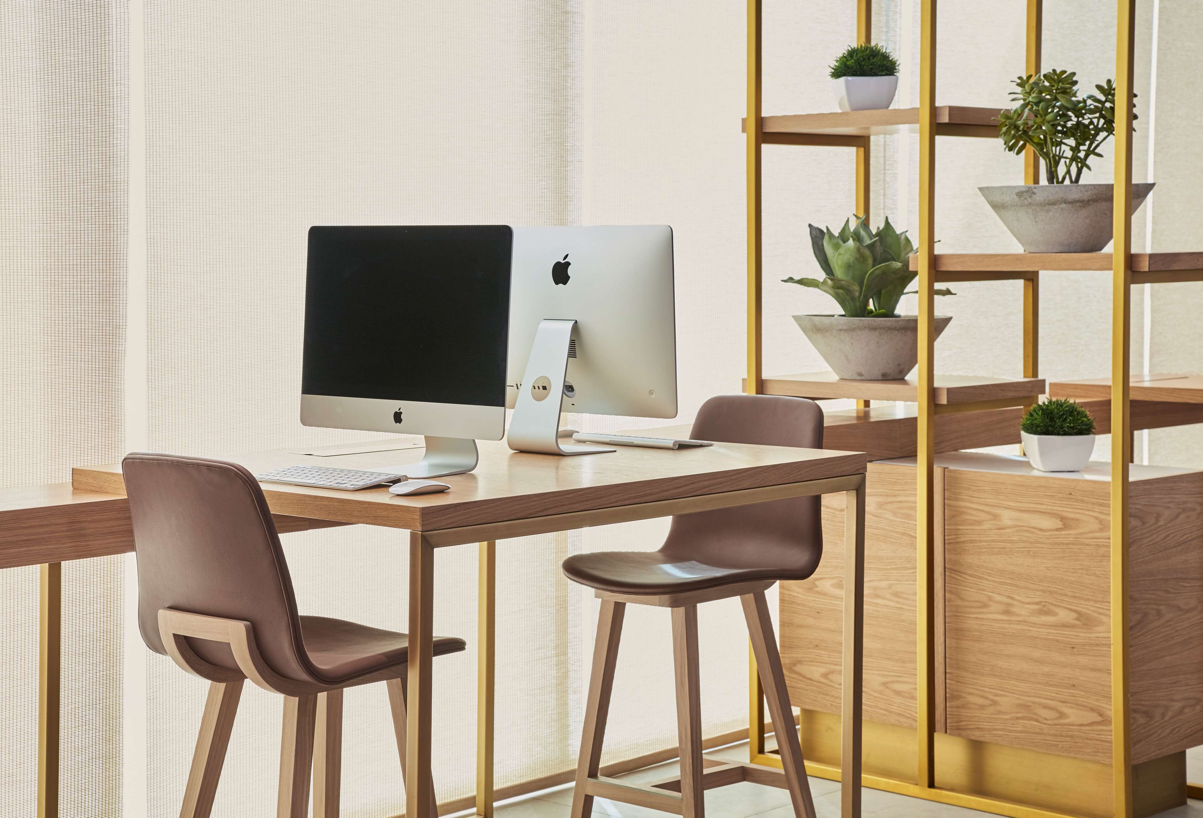 Un espace de travail moderne avec un bureau en bois, deux chaises marron, un ordinateur Apple iMac blanc et une étagère en bois agrémentée de plantes en pot.