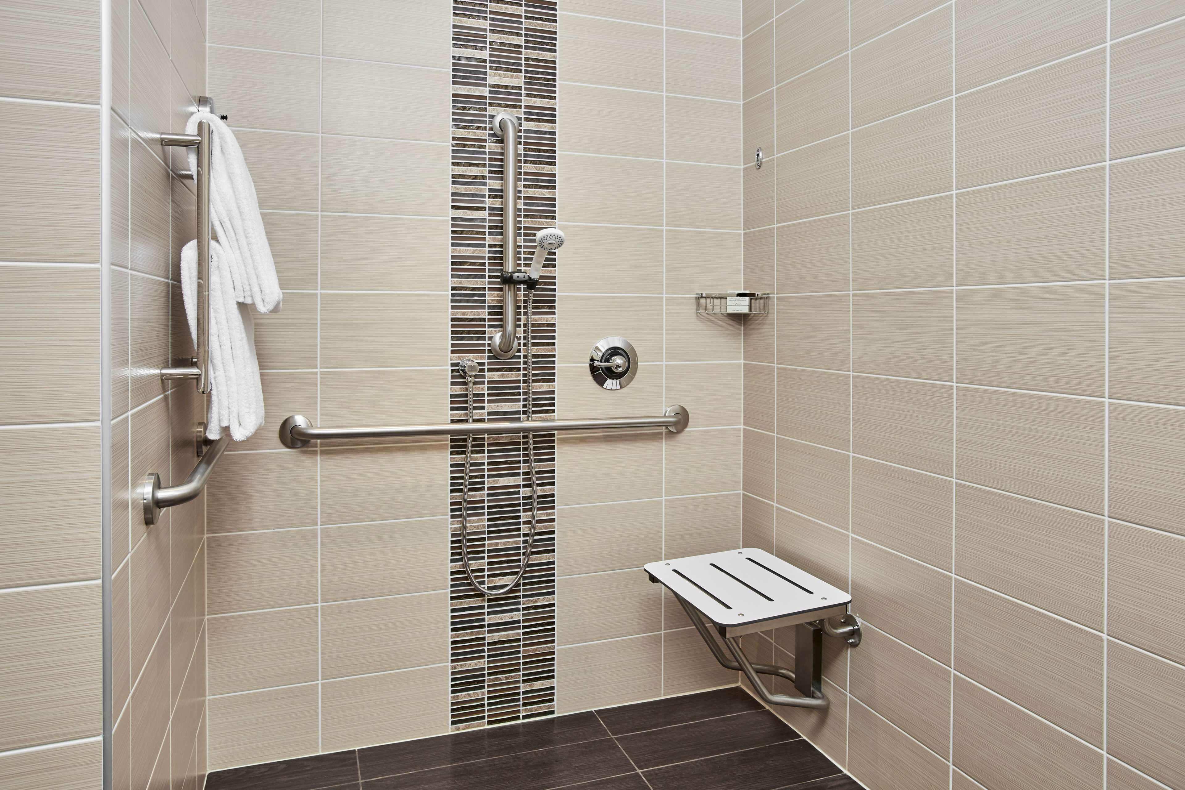A bathroom with a shower, grab bars, a towel rack, and a small sink.