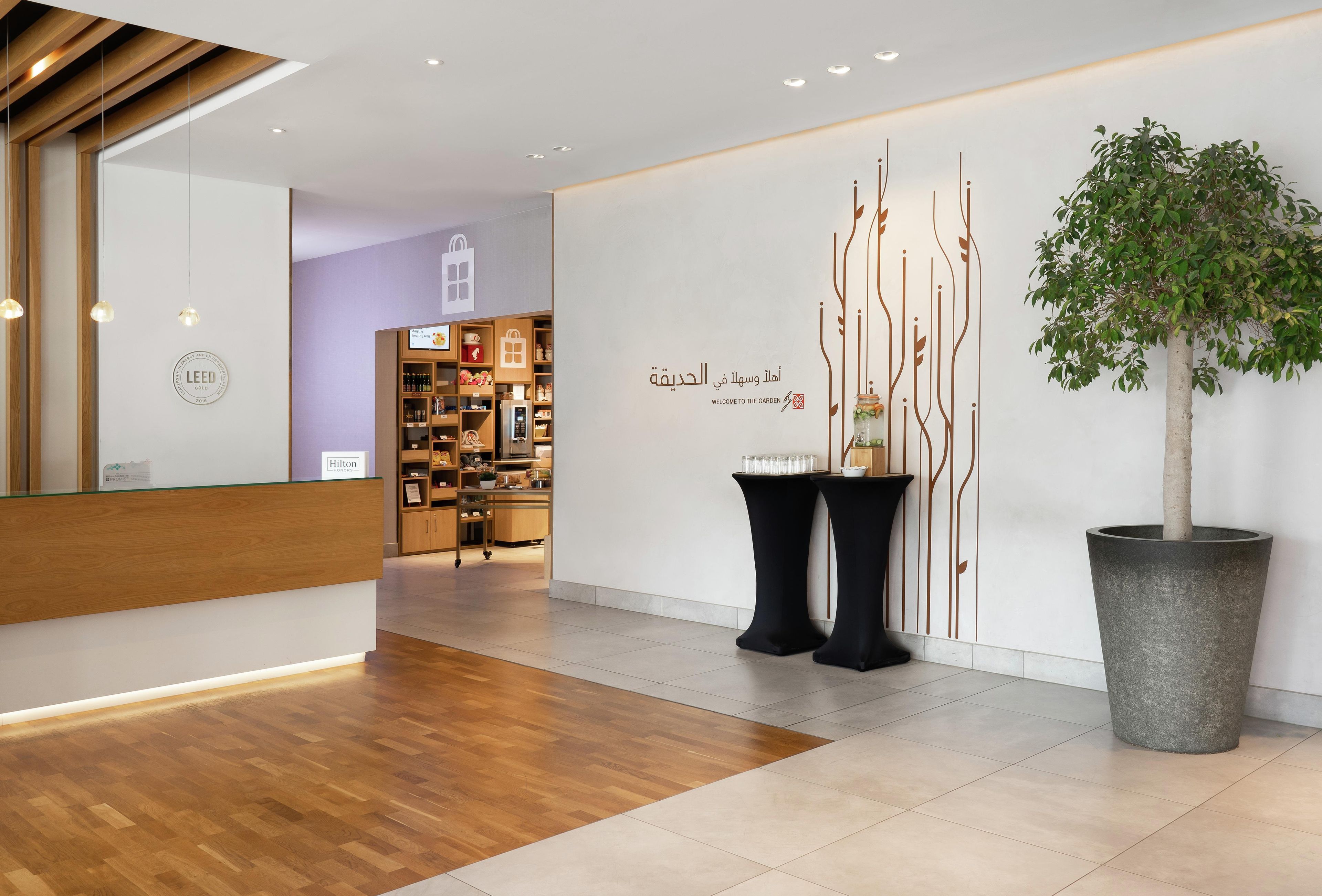 A hotel reception area with a wooden reception desk, a large potted plant, and a wall with a decorative design and text.