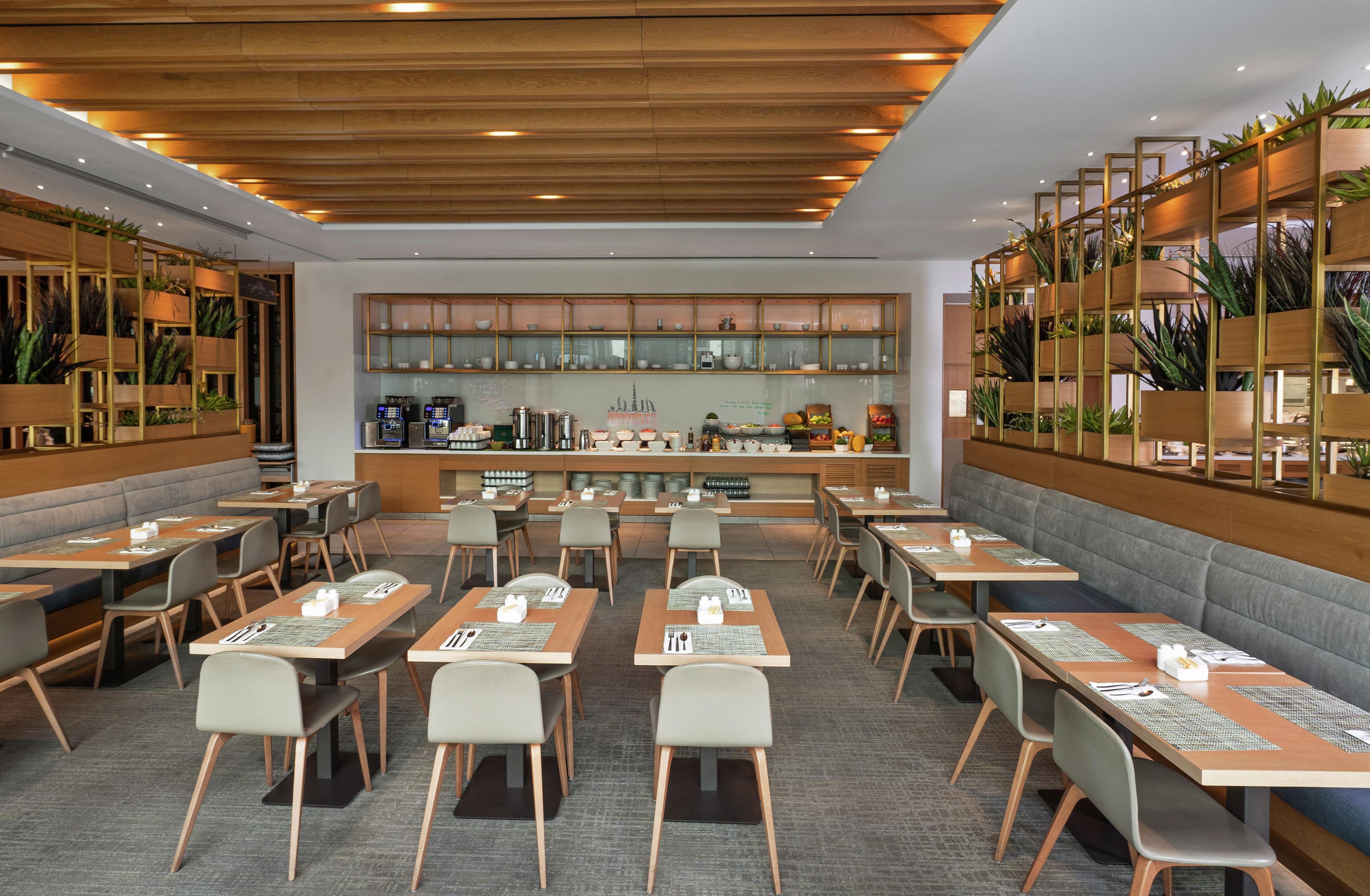 A modern restaurant with multiple tables and chairs, a coffee bar, and decorative plants.