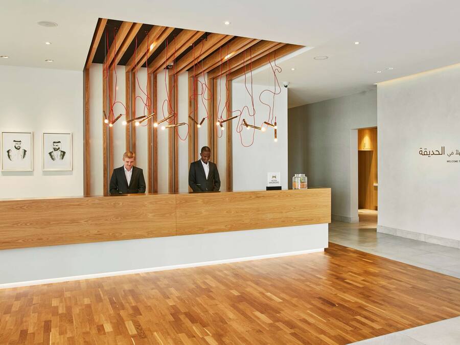 A reception area with a wooden reception desk, two staff members, and a wall with Arabic text.