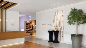 A hotel reception area with a modern design, featuring a wooden reception desk, a large potted plant, and a wall with a decorative tree and text.
