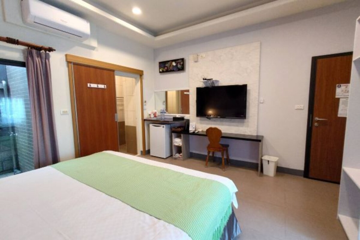 A hotel room with a bed, a desk with a computer, a TV, and a small refrigerator.
