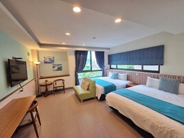 Quarto de hotel com duas camas, televisão, escrivaninha e janela com cortinas.