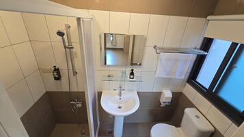 A modern bathroom with a glass shower enclosure, a pedestal sink, a toilet, and a window providing natural light.