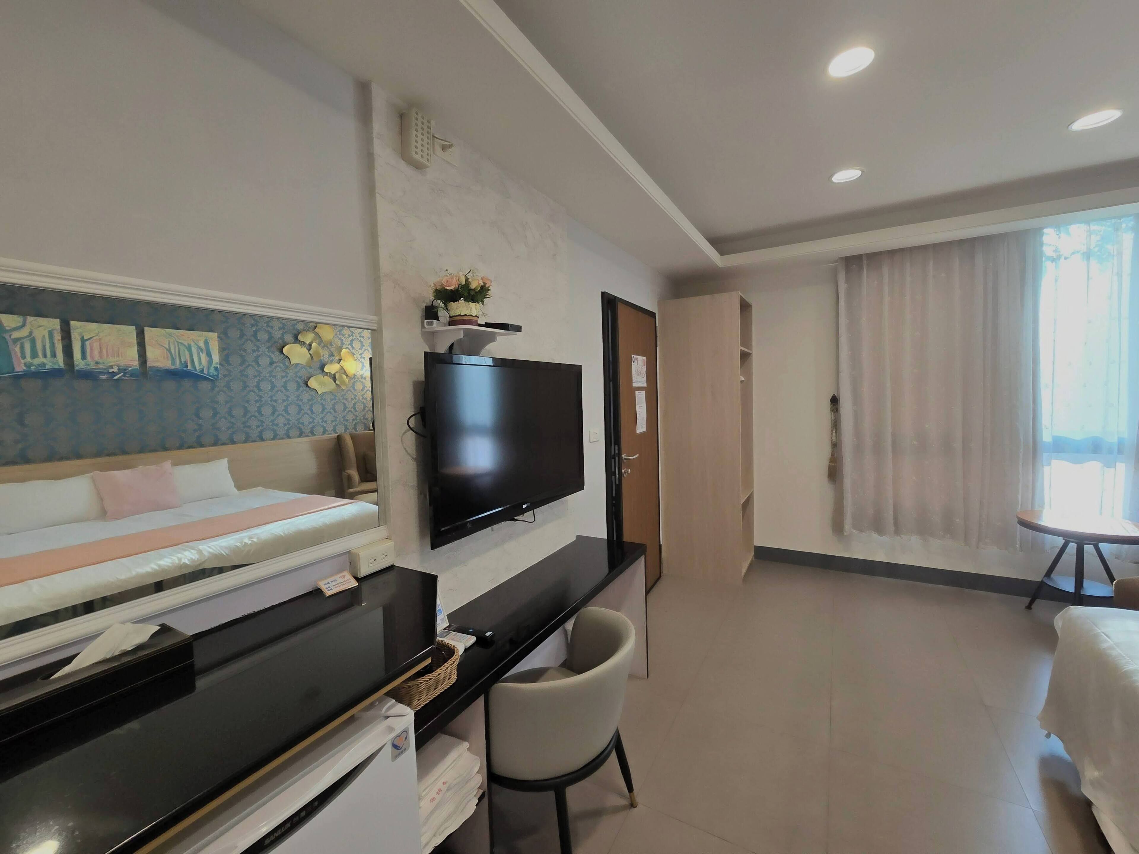 Ein Hotelzimmer mit Bett, Schreibtisch mit Computer, Fernseher, Stuhl und Fenster mit Vorhängen.