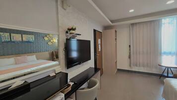 Ein Hotelzimmer mit Bett, Schreibtisch mit Computer, Fernseher, Stuhl und Fenster mit Vorhängen.