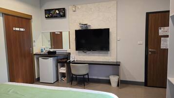 A hotel room with a bed, a desk with a computer, a television, a small refrigerator, a trash bin, and a mirror.