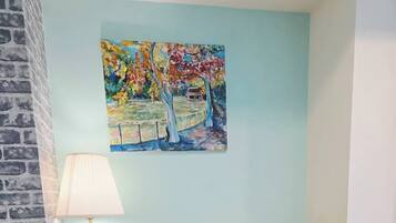 Una habitación con un sillón amarillo, una pequeña mesita de madera, una lámpara de pie y un cuadro llamativo en la pared.