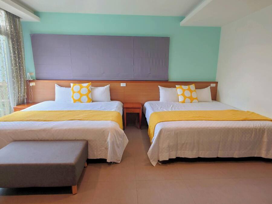 A hotel room with two beds, a wooden headboard, and a bench.