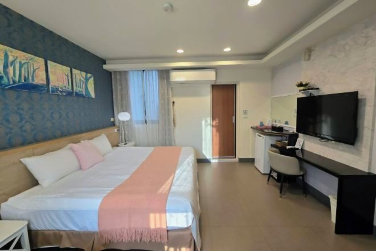 A hotel room with a bed, a desk, a television, and artwork on the wall.