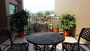 A balcony with a round metal table and four chairs, surrounded by potted plants and a view of distant buildings. - Bestime BnB (Jiji)