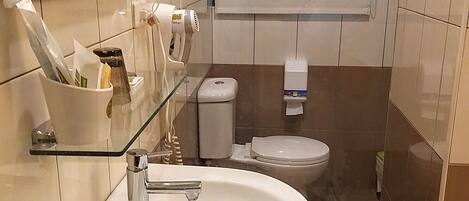 A bathroom with a white sink, a toilet, and a glass shelf with toiletries.