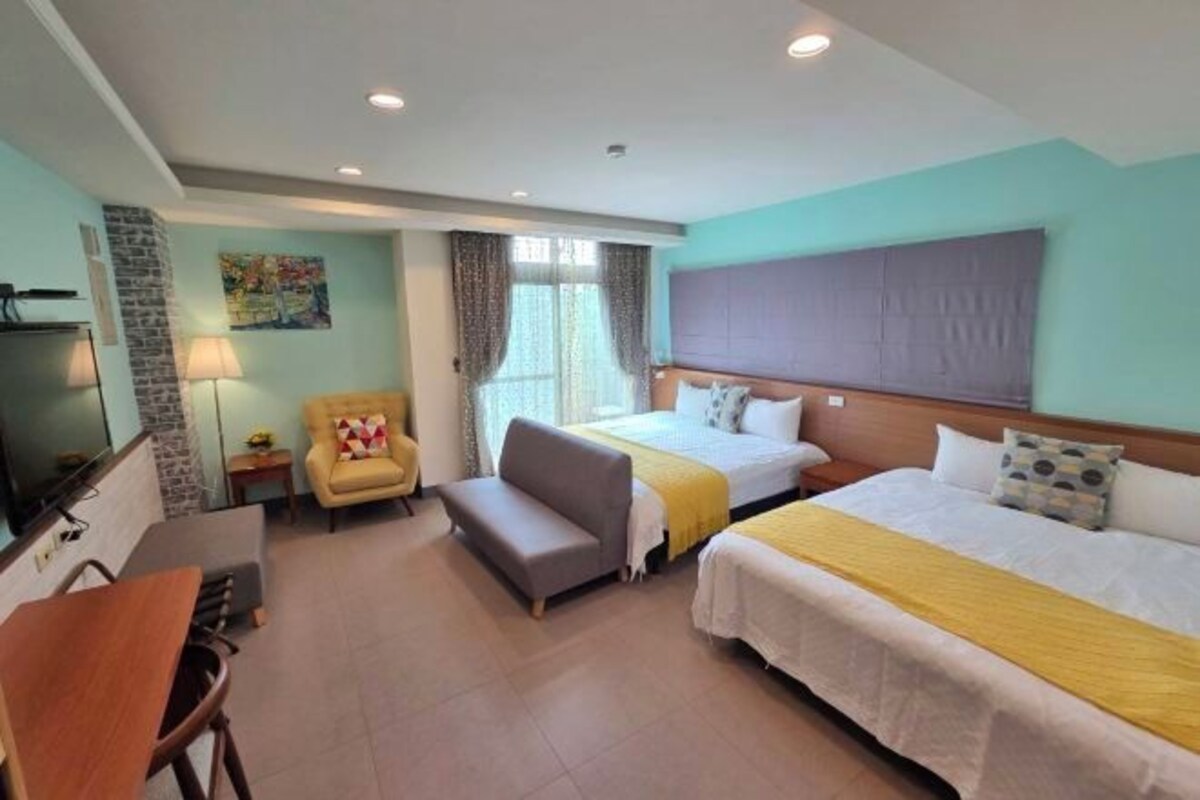A hotel room with two beds, a sofa, a TV, and a dining table.